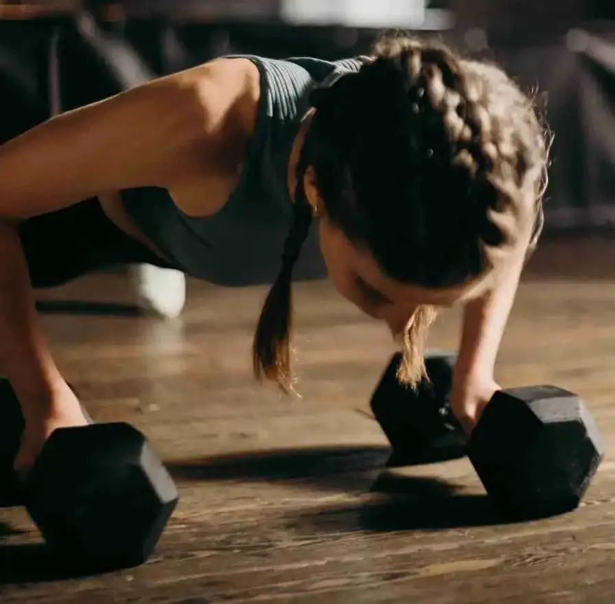 تصویر یک زن ورزشکار در حال اجرای تمرینات متناوب HIIT با دمبل